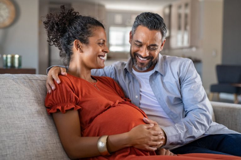 Homem fazendo carinho na barriga de sua esposa grávida. eles estão sentados no sofá e sorrindo