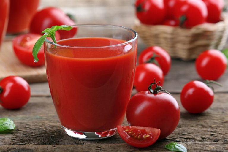 Copo de vidro com suco de tomate em cima de uma mesa com tomates-cereja 