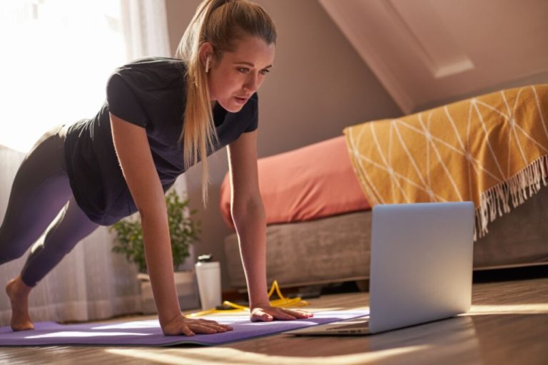 Mulher fazendo exercício em casa e em frente a um notebook