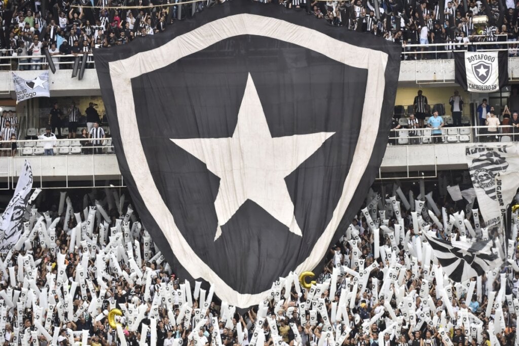 bandeira grande com brasão do botafogo estendida sobre arquibancada em estádio