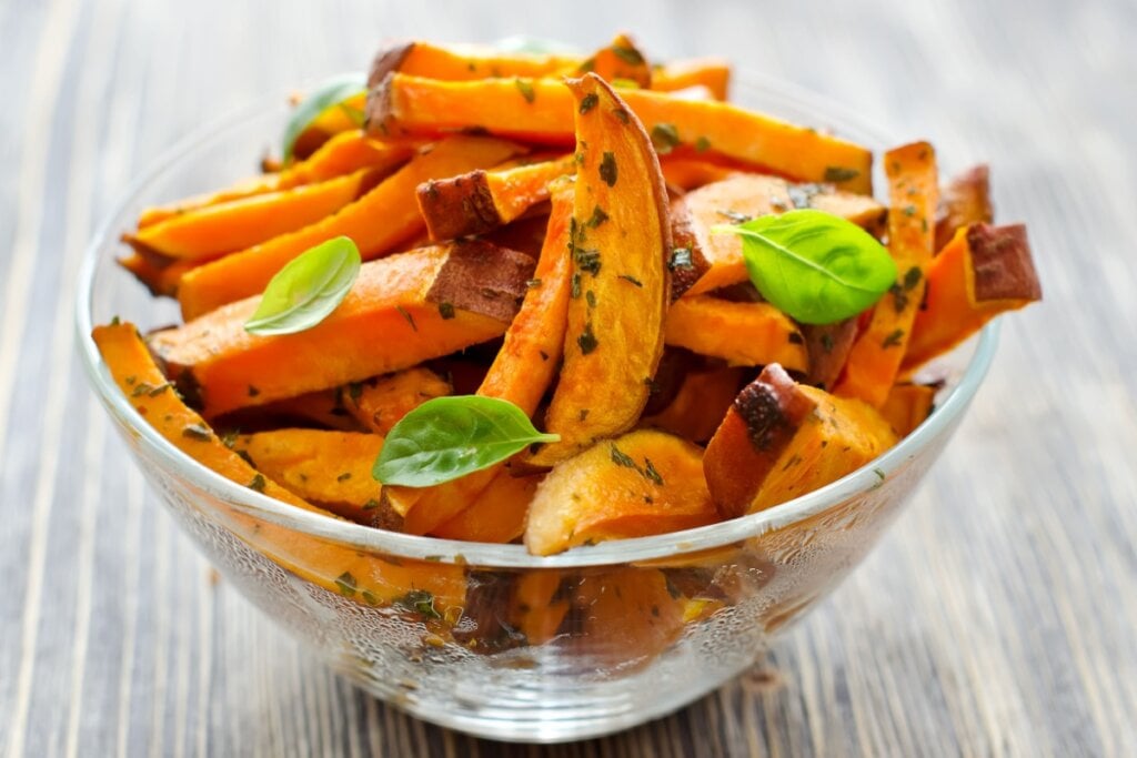 recipiente de vidro com palitos de batata-doce laranja assada com ervas e folhas de manjericão