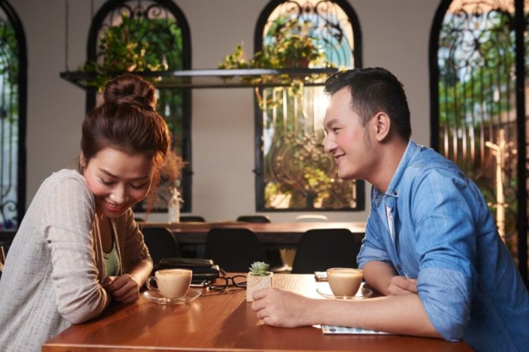 Homem e mulher tomando um café sorrindo um para o outro e com bochechas vermelhas