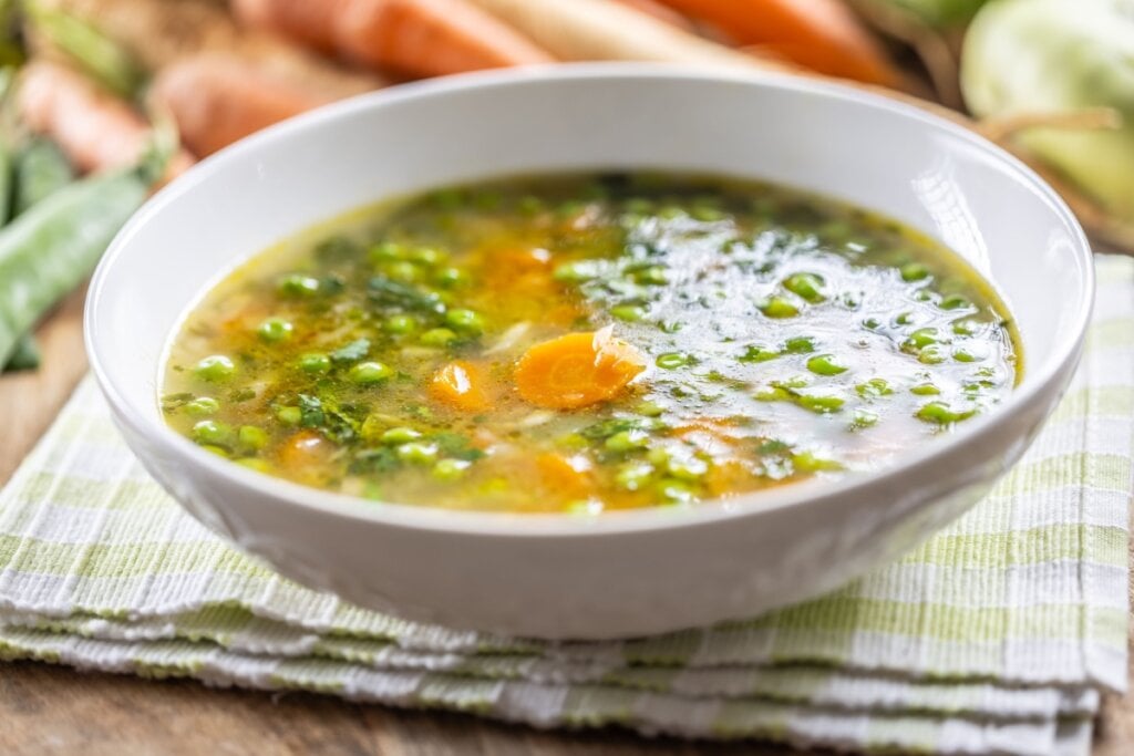 Caldo de ervilha e cenoura servido em tigela funda de cerâmica em cima de pano de prato e em cima de mesa de madeira
