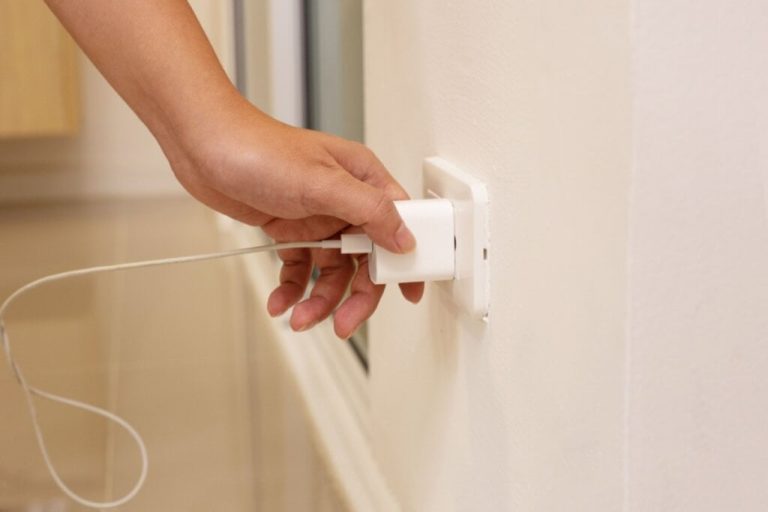 Mão tirando um carregador branco de celular de uma tomada 