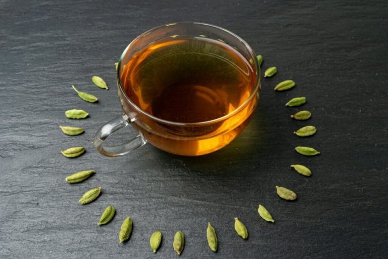 Xícara de vidro em cima de uma mesa preta rodeada por sementes de cardamomo