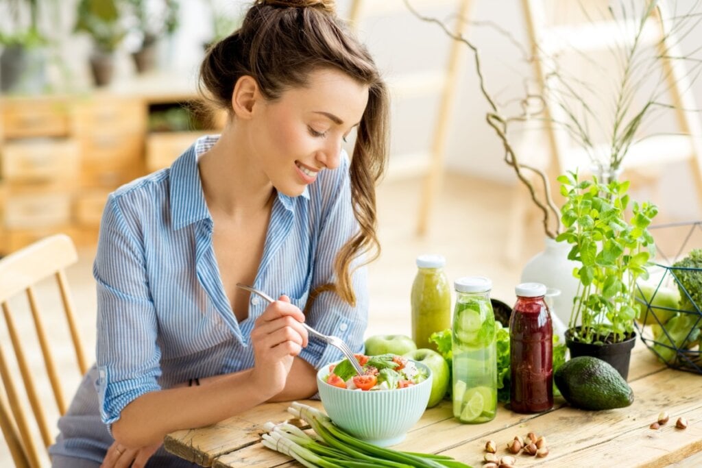 Mulher sentada e comendo salada em um recipiente branco