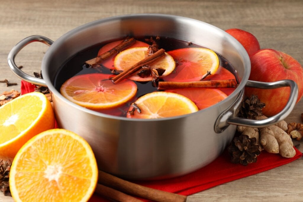 Panela de metal com vinho quente, rodelas de laranja, canela em pau e anis-estrelado em cima de um pano vermelho