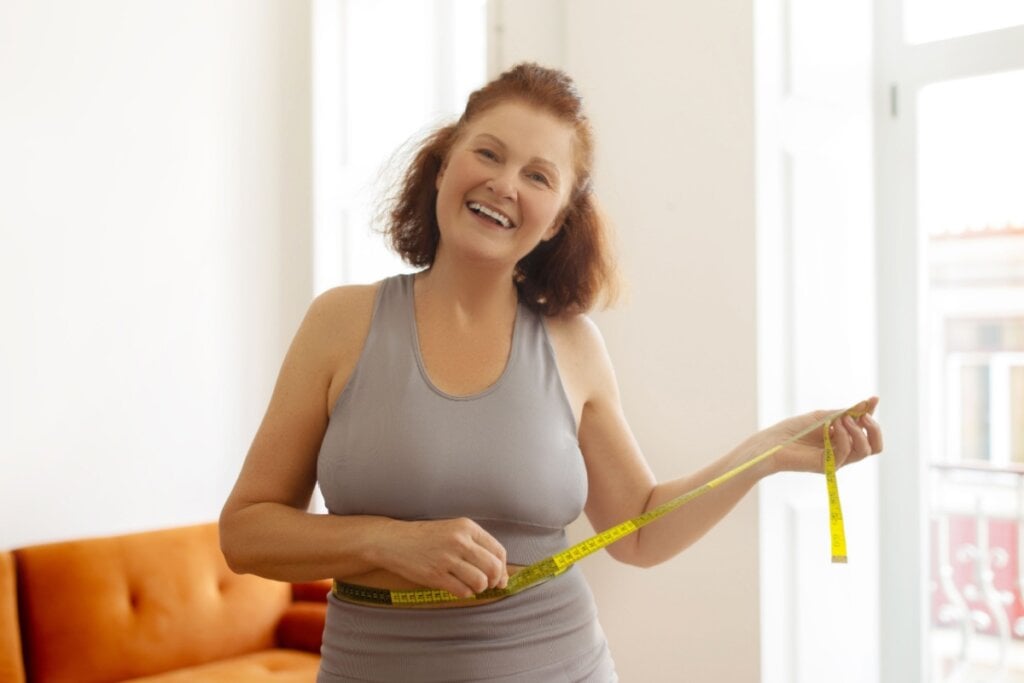 Mulher de meia-idade, sorrindo e segurando uma fita métrica na cintura