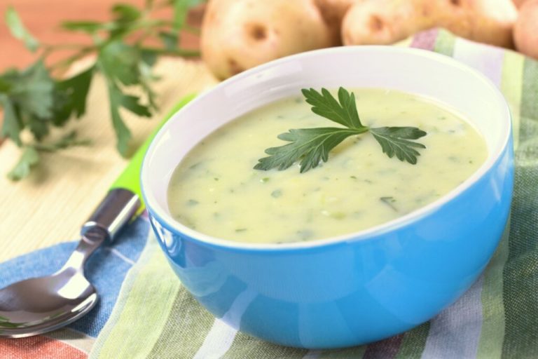 Recipiente azul com creme de batata em cima de uma mesa com uma colher e batatas