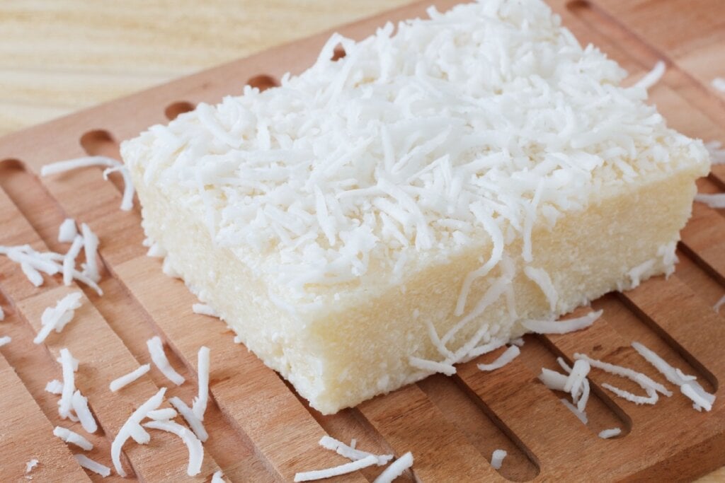 Pedaço de cuscuz de tapioca, polvilhado com coco ralado, em cima de uma tábua de madeira