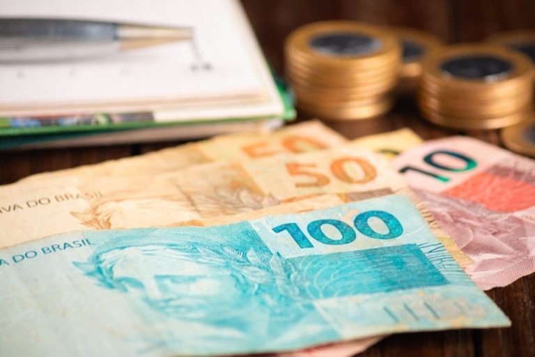 imagem de notas de 100, 50 e 10 reais juntas e com moedas ao fundo