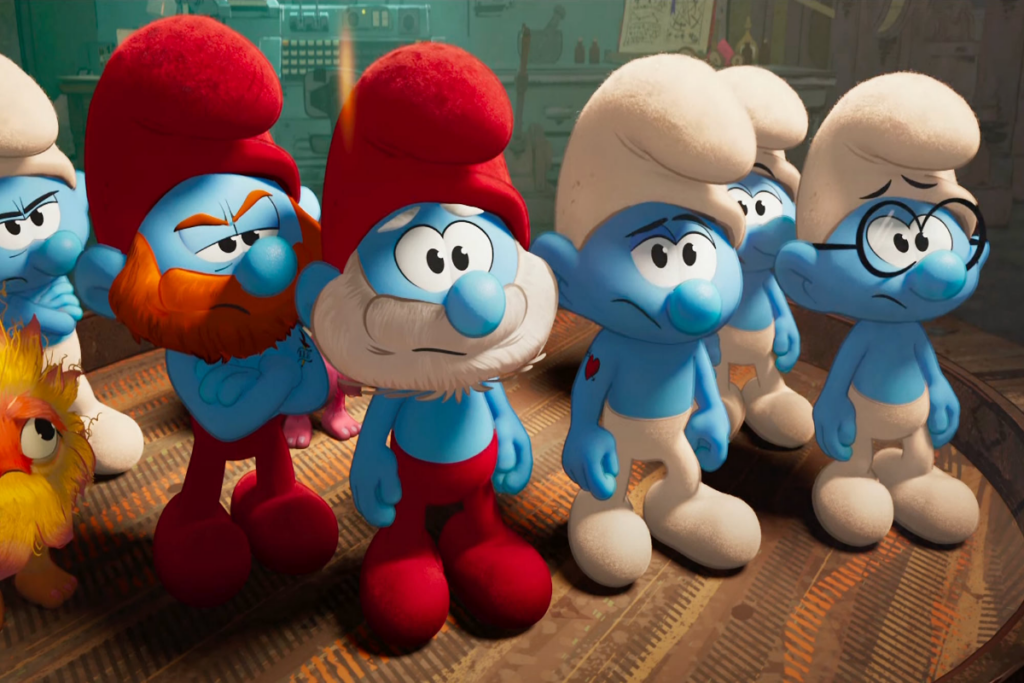 Ilustração de personagens pequenos azuis, 4 estão usando gorros e calças brancas e um deles está usando gorro e calça vermelha e tem o cabelo e a barba branca e outro está usando gorro vermelho e tem a barba ruiva