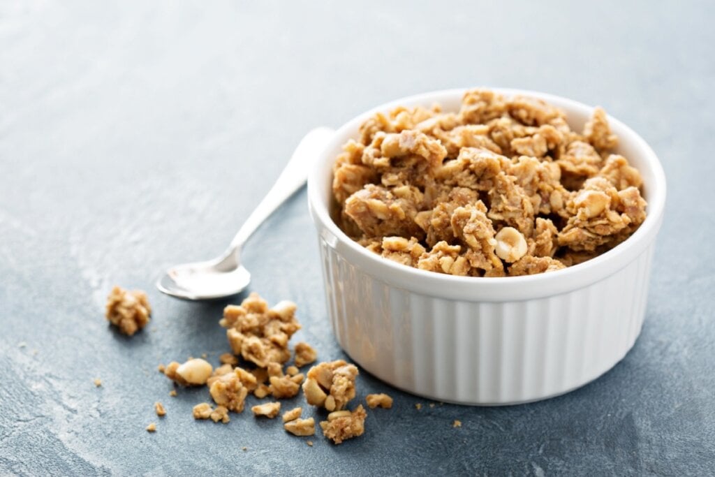 pote branco com granola com amendoim e colher de metal ao lado