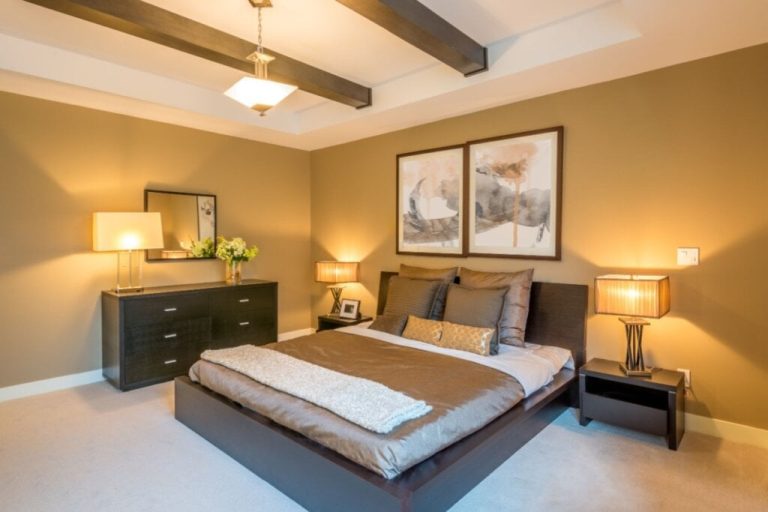 Quarto com parede bege-claro, luzes amarelas e uma cama com forro cinza e branco