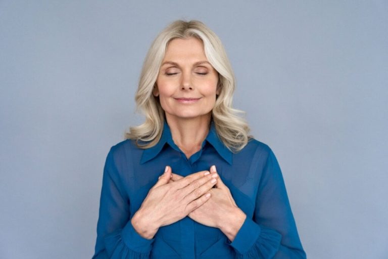 Mulher de meia-idade de olhos fechados sorrindo com mãos no peito
