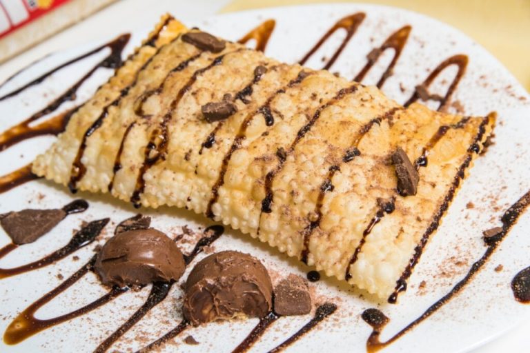 Pastel decorado com calda de chocolate e bombons em cima de um prato branco