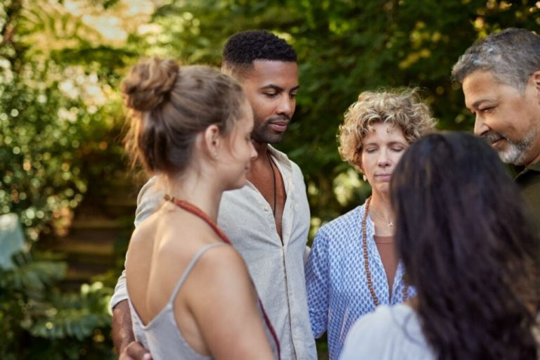 homens e mulheres reunidos em círculo e com os olhos fechados