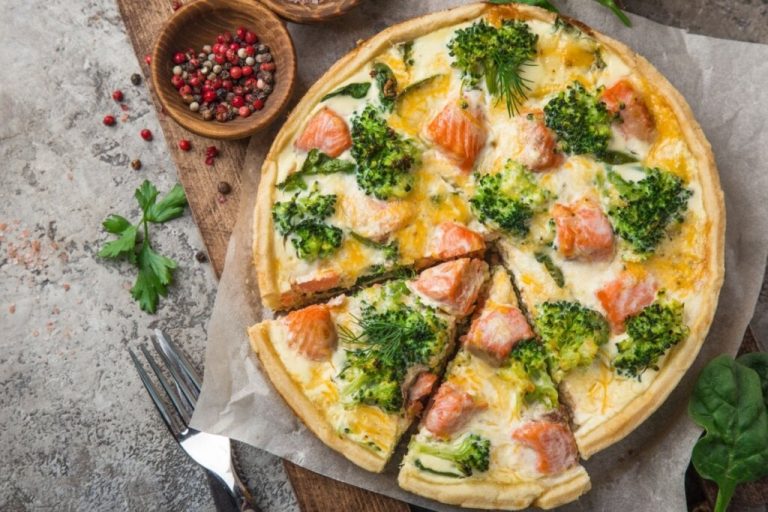 Quiche de salmão com brócolis em cima de um papel-manteiga em uma mesa cinza 