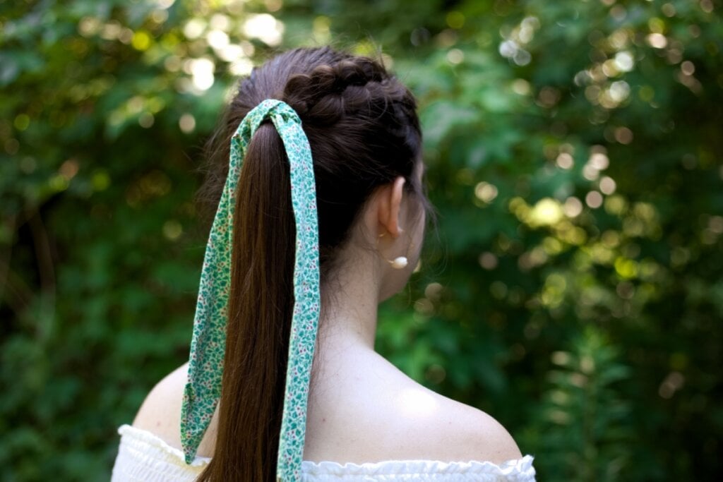 Mulher virada de costas, com o cabelo em rabo de cavalo, trança embutida e um laço verde