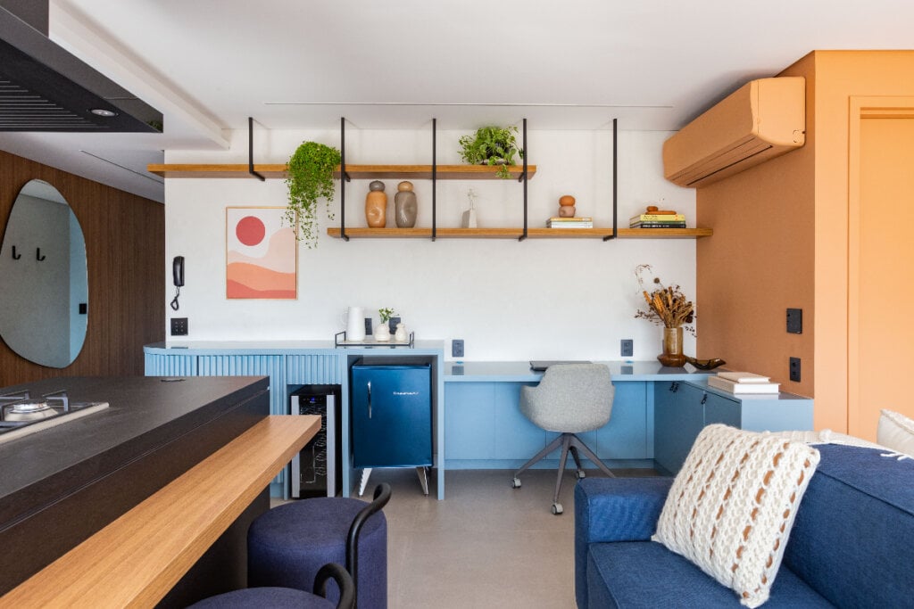 imagem de sala de estar com sofá e poltronas azuis com bar e home office com armário azul-claro ao fundo e cadeira cinza