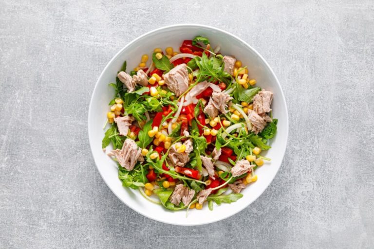 prato branco com salada de atum, rúcula, milho-verde e pimentão em fundo cinza