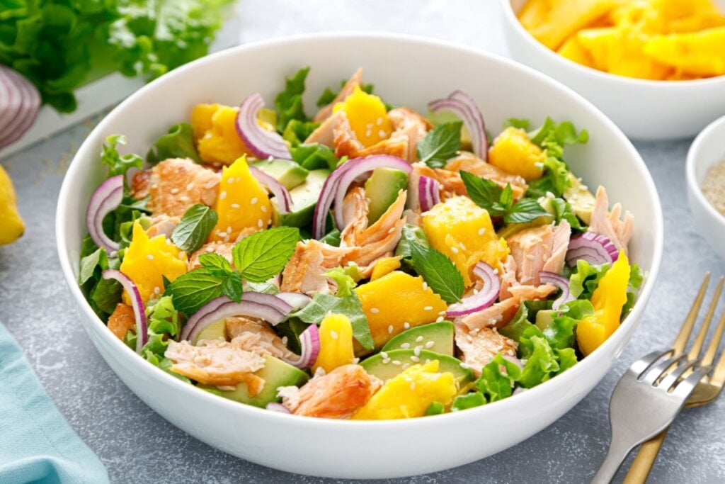 Salada de salmão com manga e abacate servido em tigela funda de cerâmica em cima de mesa de pedra