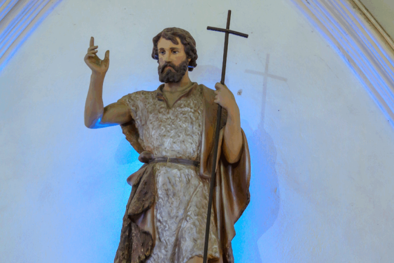 Estátua de São João segurando uma cruz e com uma das mãos levantadas 