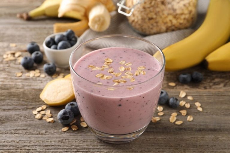 Copo de vidro com shake de blueberry decorado com flocos de aveia 