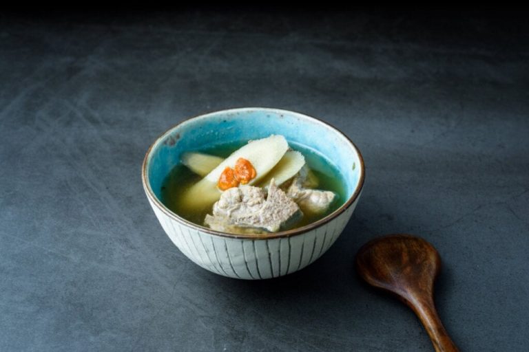 recipiente azul com sopa de inhame e costelinha de porco. colher de pau ao lado