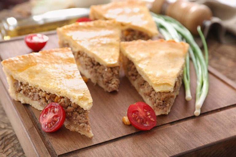 Quatro pedaços de torta com carne moída em cima de uma tábua de madeira 