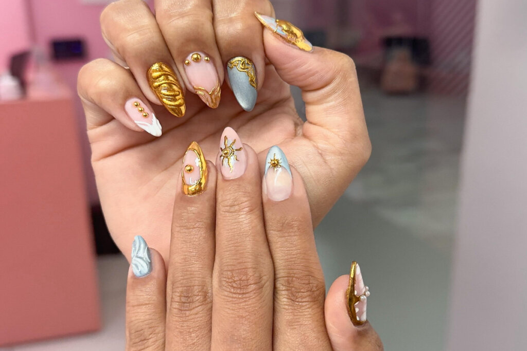duas mãos com unhas em tons de amarelo, azul e rosa com aplicações 3D