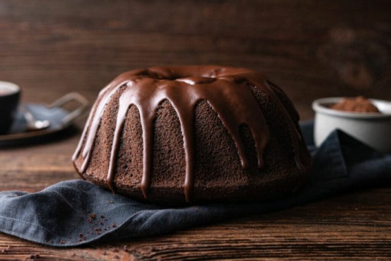 Mesa de madeira com um bolo de chocolate com cobertura em cima de um pano azul