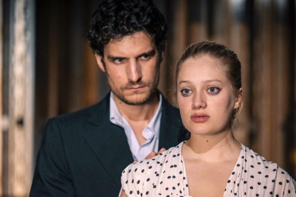 Homem e mulher em pé e olhando para a frente em cena do filme "Jovens Amantes"