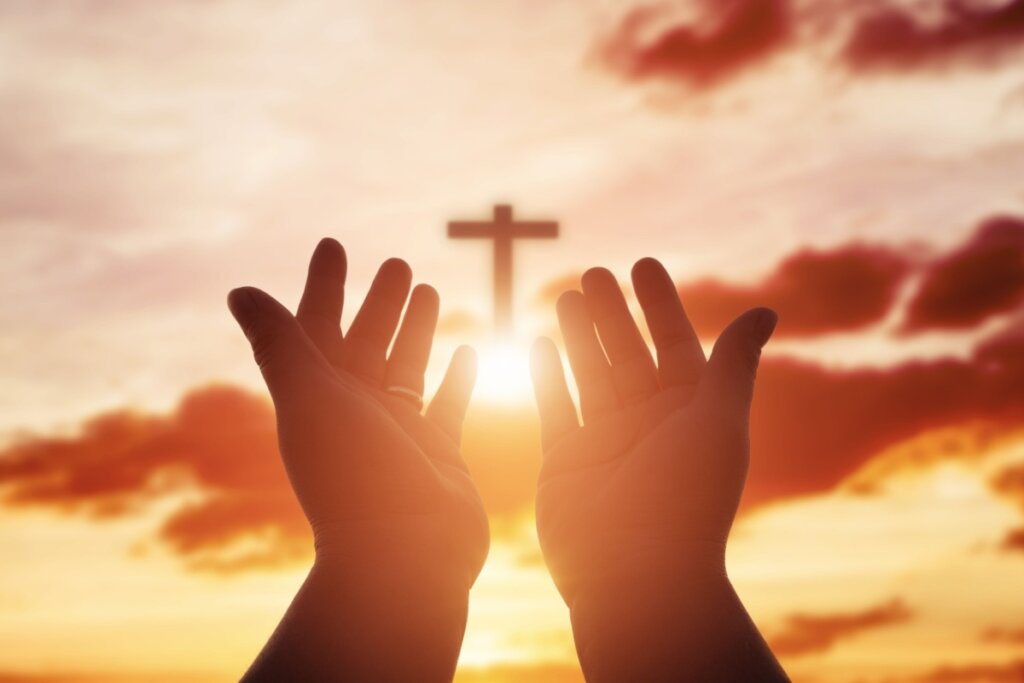 Mãos humanas apontadas para o céu e cruz no meio