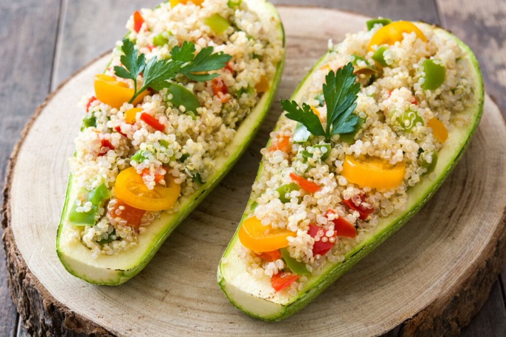 Abobrinha recheada com quinoa e pimentão servido em tábua de madeira em cima de mesa de madeira
