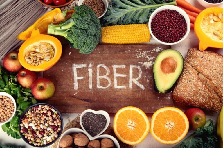Alimentos com fibras dispostos em mesa de madeira e no centro uma plaquinha em madeira escrito de giz a palavra fiber