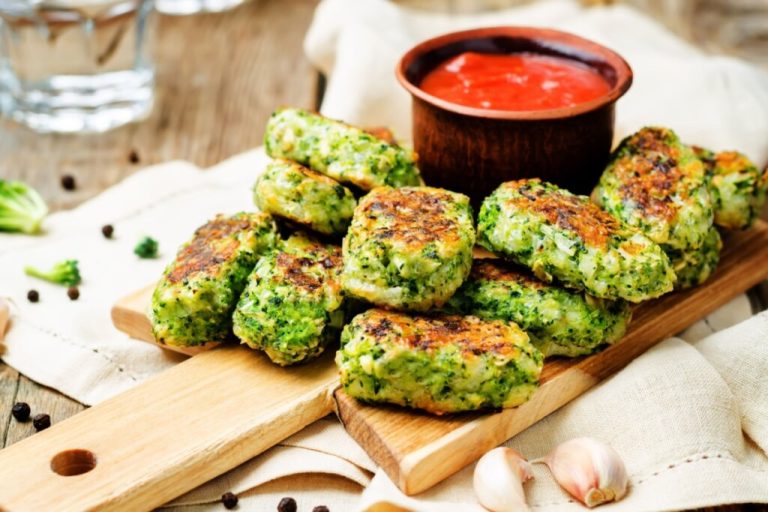 Bolinhos de brócolis em cima de uma tábua de madeira com um recipiente com molho ao lado 