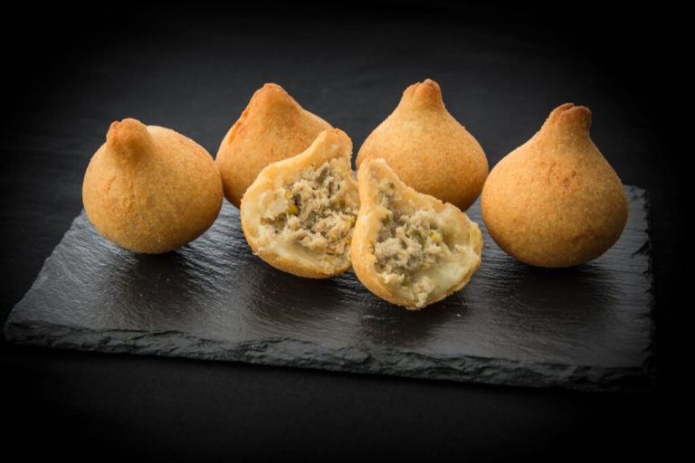 Coxinha de carne de jaca em cima de travessa retangular preta de pedra em cima de mesa preta