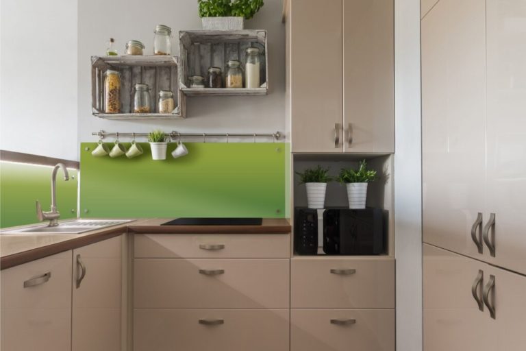 Cozinha pequena com móveis modulados na cor bege, com parede acima do balcão em verde