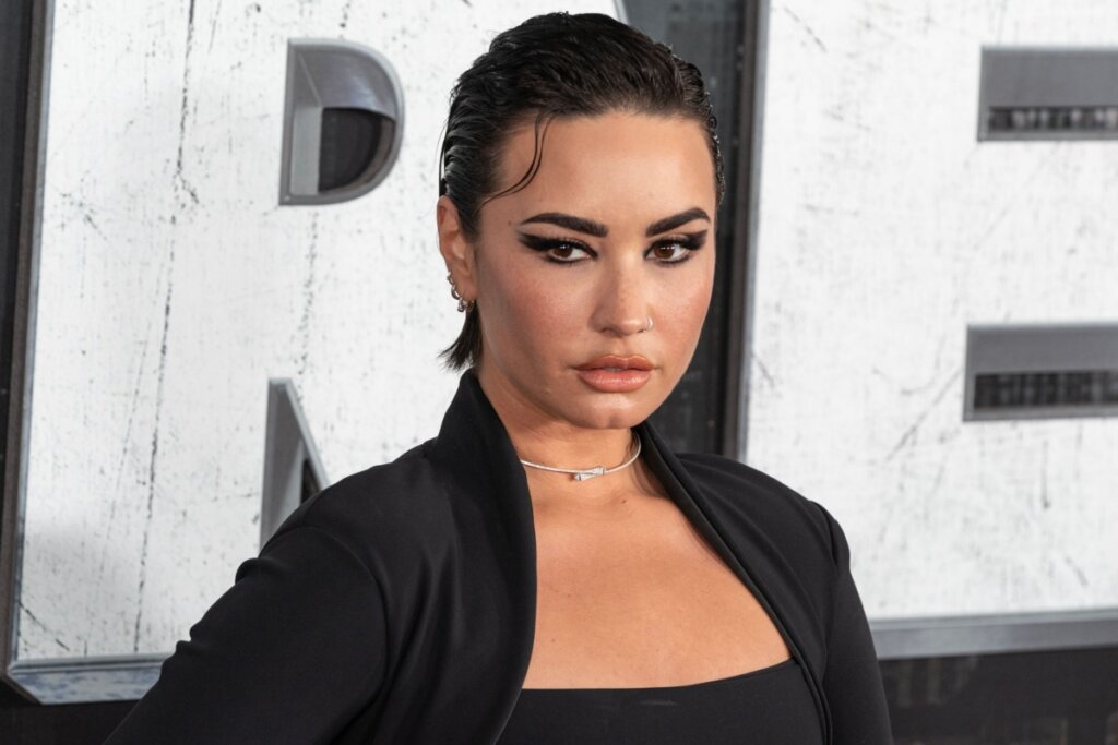 Mulher com o cabelo curto preso com gel e usando maquiagem preta e vestido preto com decote quadrado posando para foto