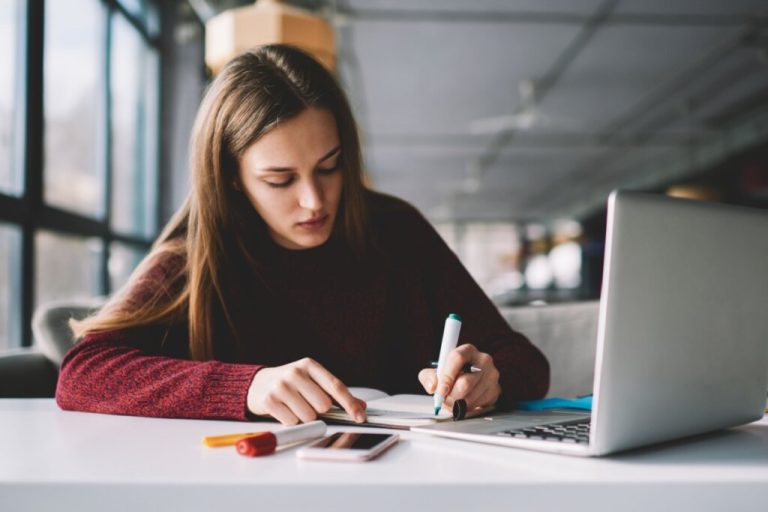 Estudante sentada e usando blusa vermelha fazendo planejamento em um papel 