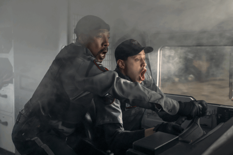 Dois homens usando uniformes pretos gritando dentro de um carro que está cheio de fumaça dentro