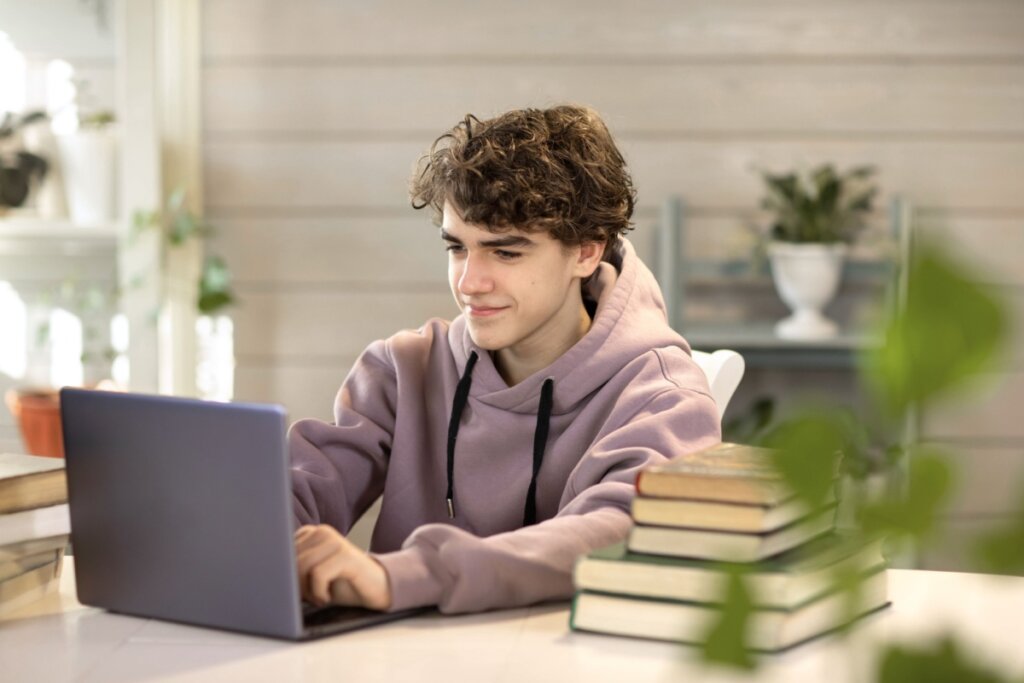 Jovem com o cabelo curto e usando blusa de moletom em roxo claro estudando no notebook