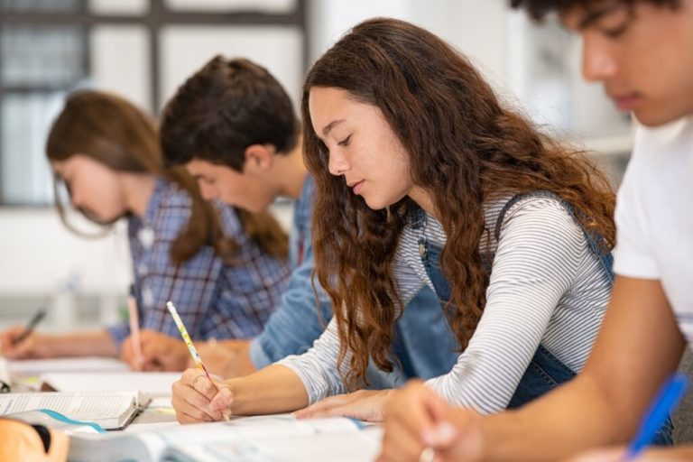 Grupo de estudantes escrevendo no caderno enquanto assistem a aula