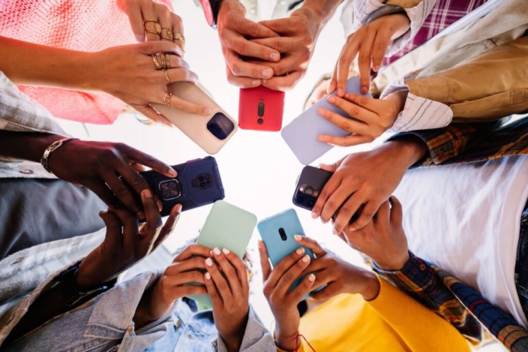 Mãos de pessoas reunidas em uma roda segurando celular