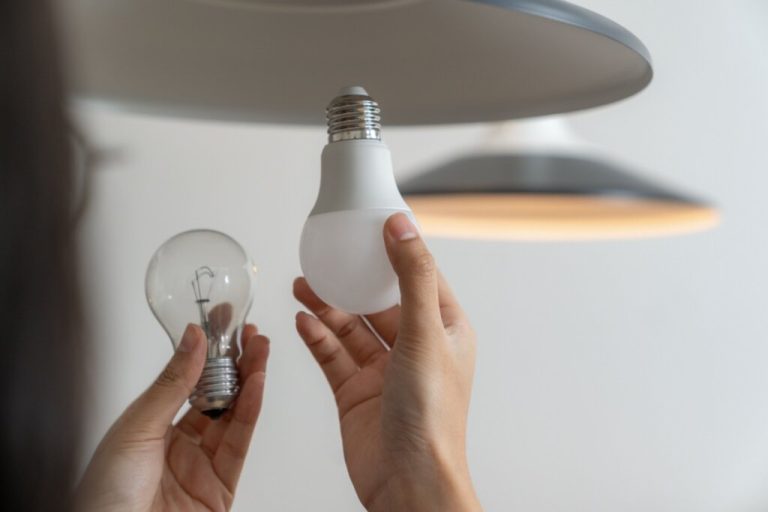 Mãos segurando duas lâmpadas, uma de LED e a outra incandescente