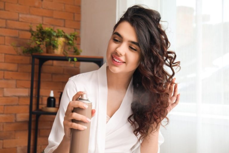 mulher de roupão branco aplicando spray no cabelo cacheado e sorrindo