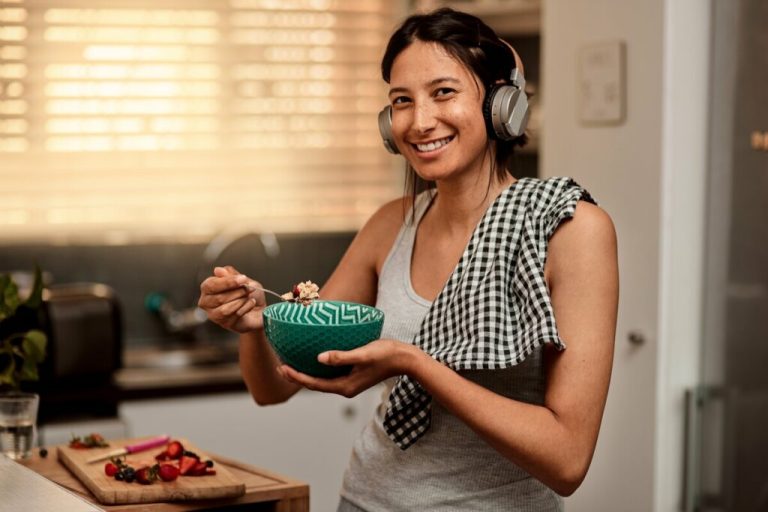 Mulher sorrindo usando fone de ouvido e segurando uma colher e uma tigela