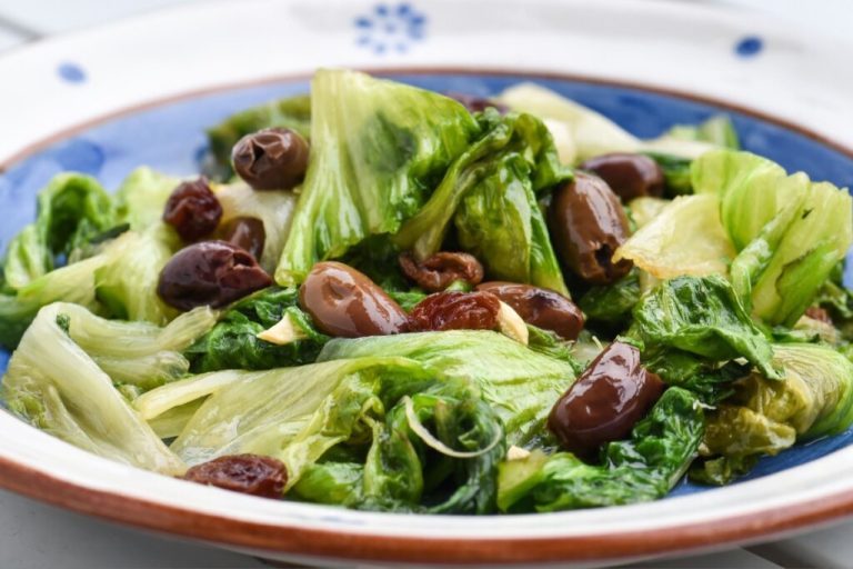 Prato azul e branco com salada com folhas de escarola e azeitonas pretas 