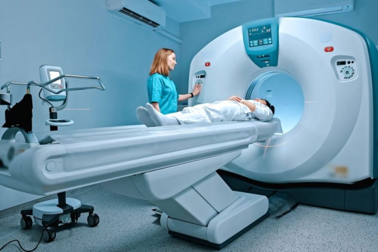 Pessoa deitada fazendo ressonância magnética e uma médica em pé do lado